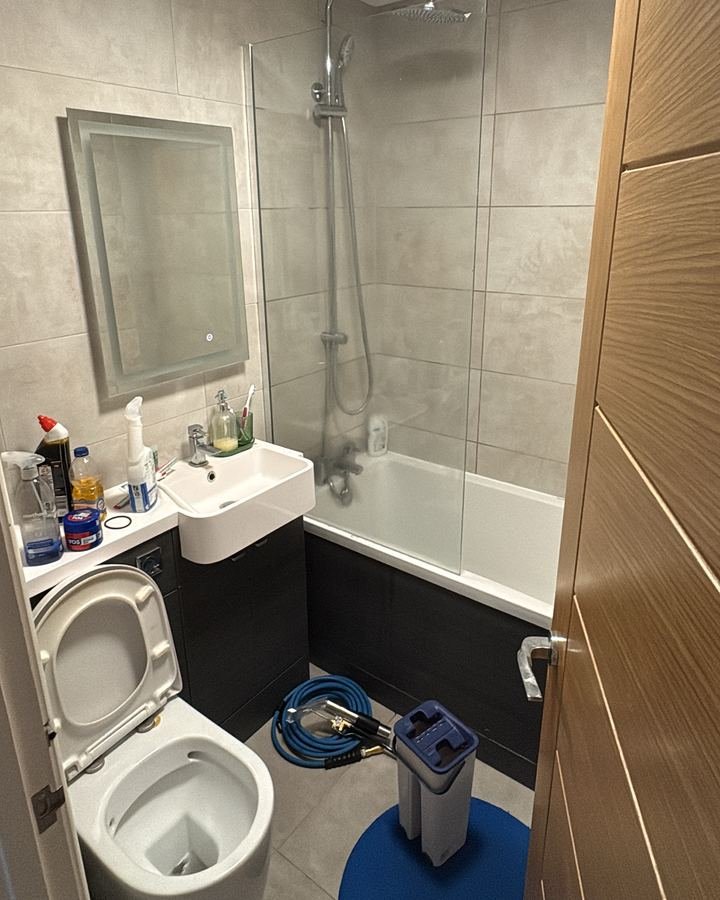 Bathroom before cleaning with products cluttering the vanity, toilet left open and dull surfaces