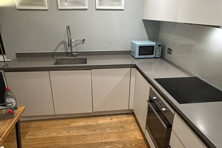 Clean modern kitchen with white cupboards, grey worktops, induction hob and wooden floor after an end-of-tenancy clean