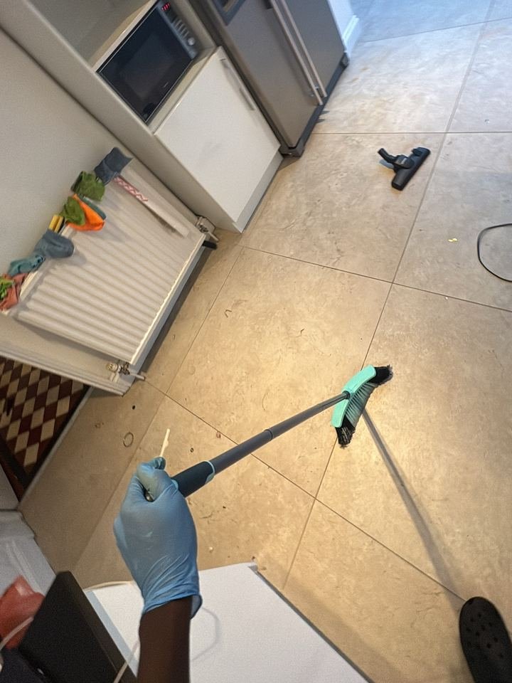 Mopford cleaner in gloves sweeping a tiled kitchen floor during a clean