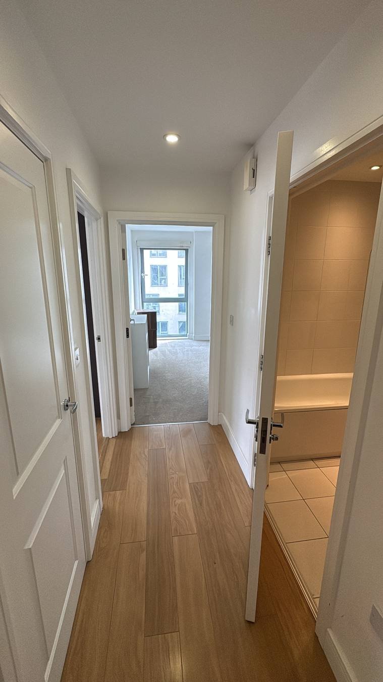 Clean hallway with oak flooring and white doors leading to a carpeted bedroom