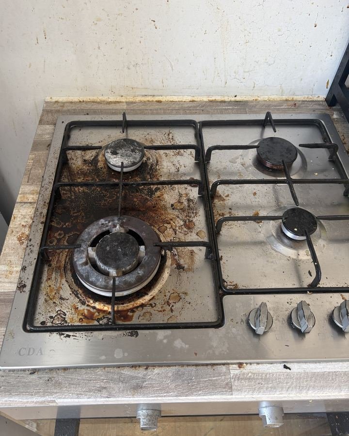 Gas hob before cleaning, covered in burnt-on grease with splattered wall behind