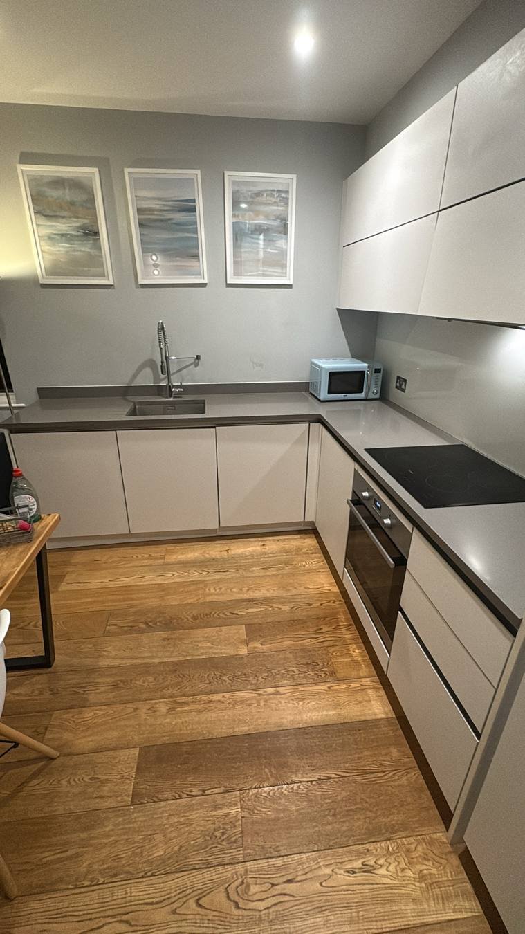 Spotless modern kitchen with white handleless cupboards, grey worktops and oak floor after a Mopford end-of-tenancy clean